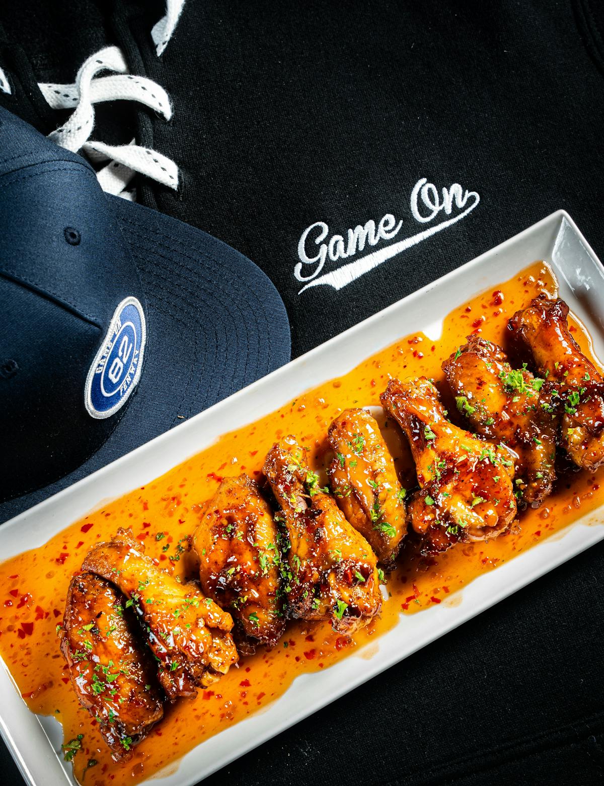 Wings in sauce on a tray beside a Game On cap