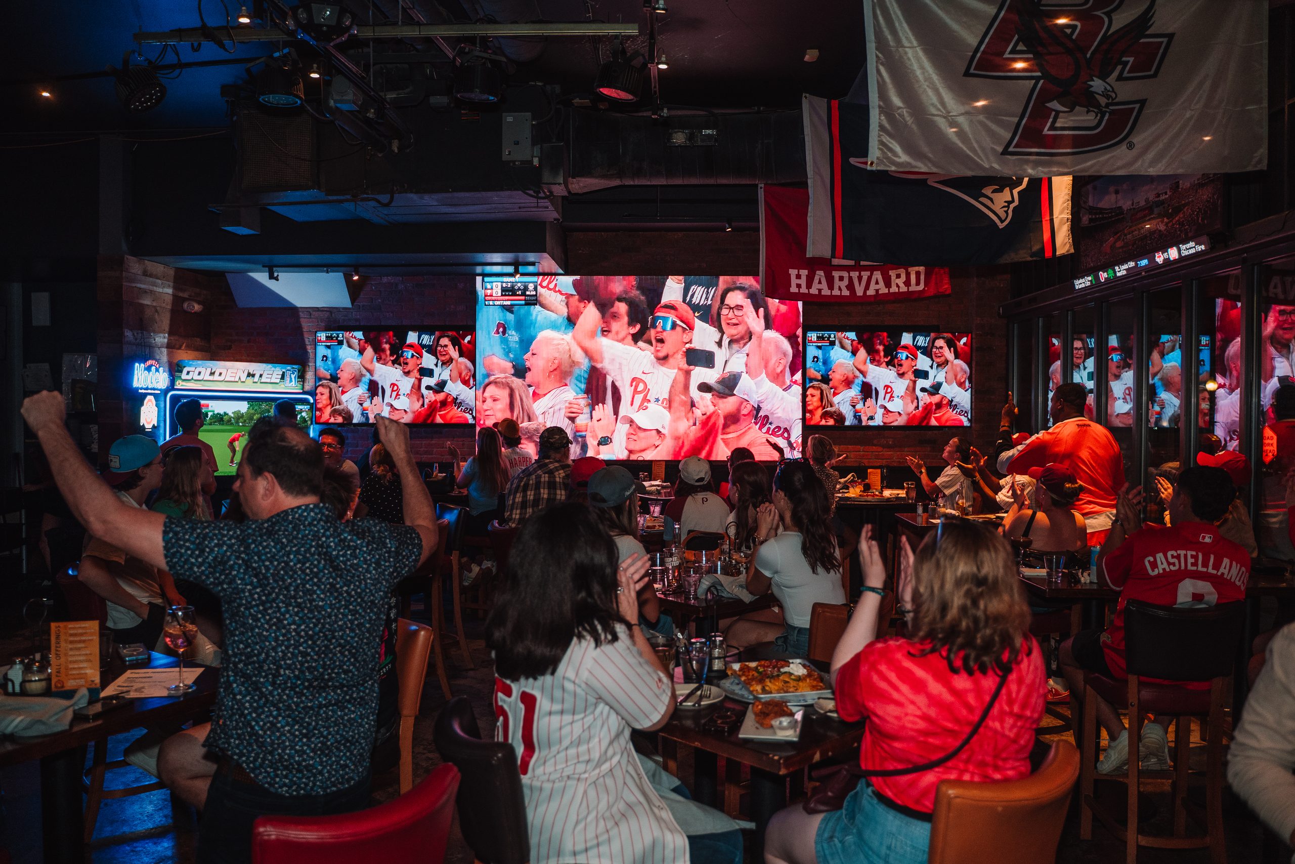 Fans at tables cheering while watching a game on Game On's big screens